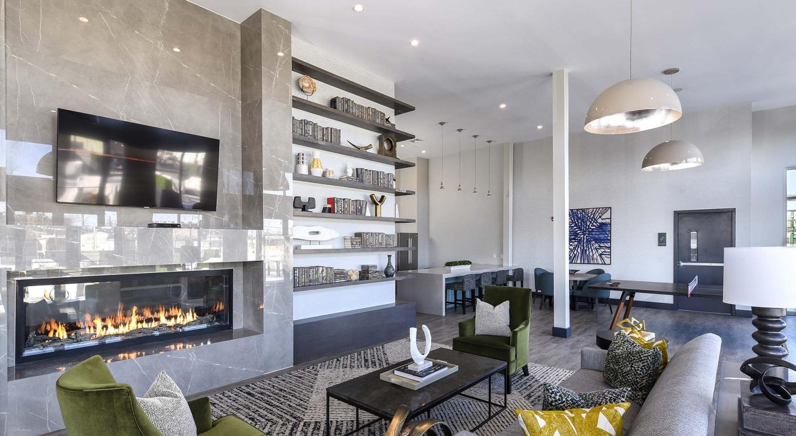 Quick access to state-of-the-art amenities a clubroom with a fireplace, a couch, tables and chairs